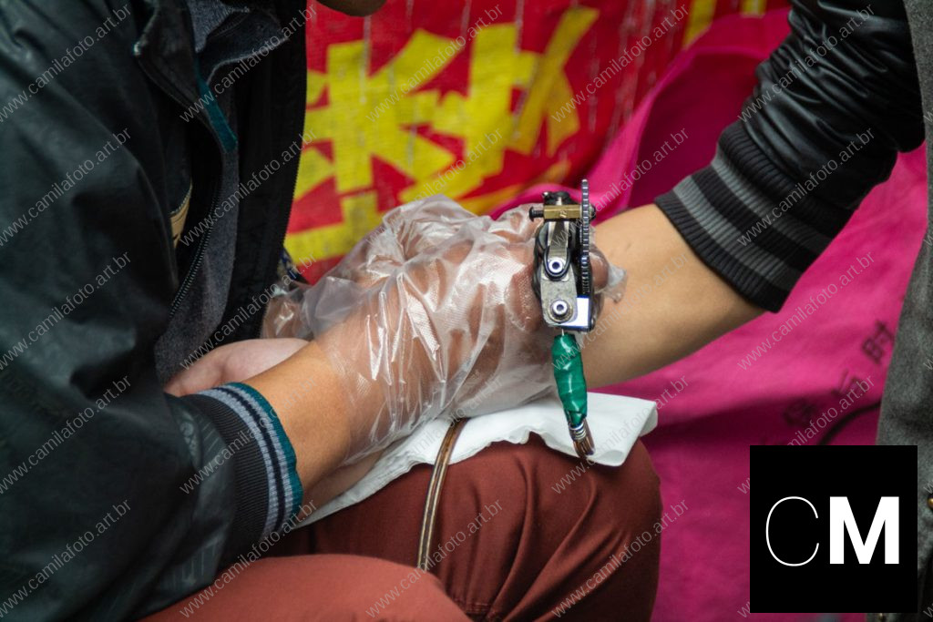 duas pessoas sentadas numa rua, sendo um tatuador e a pessoa que está sendo tatuada. 100 CNY é parte da série outras estórias por Ca Mila
