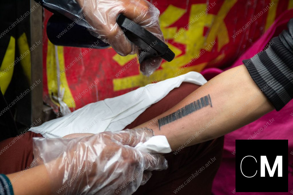 duas pessoas sentadas numa rua, sendo um tatuador e a pessoa que está sendo tatuada. 100 CNY é parte da série outras estórias por Ca Mila