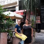 duas pessoas posando para a foto em frente a um restaurante. américa é parte da série (pop)ulares por Ca Mila