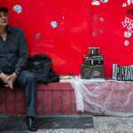 um vendedor ambulante sentado ao lado de seus produtos. américa é parte da série (pop)ulares por Ca Mila