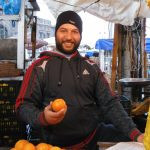 um vendedor de feira livre posando para a foto segurando uma laranja. áfrica é parte da série (pop)ulares por Ca Mila