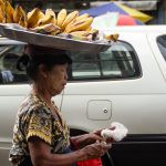 uma vendedora ambulante andando na rua equilibrando uma cesta com bananas. ásia é parte de (pop)ulares por Ca Mila.