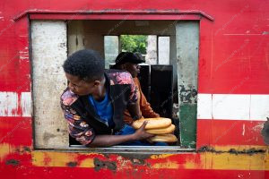 uma pessoa sentada na janela do trem segurando pães. 163 km é parte da série outras estórias por Ca Mila