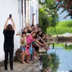 uma pessoa fazendo foto de outras pessoas numa fila. coletivo é parte de emoções por Ca Mila