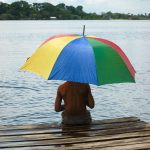 uma pessoa sentada numa plataforma com um guarda-chuva. serenidade é parte de emoções por Ca Mila